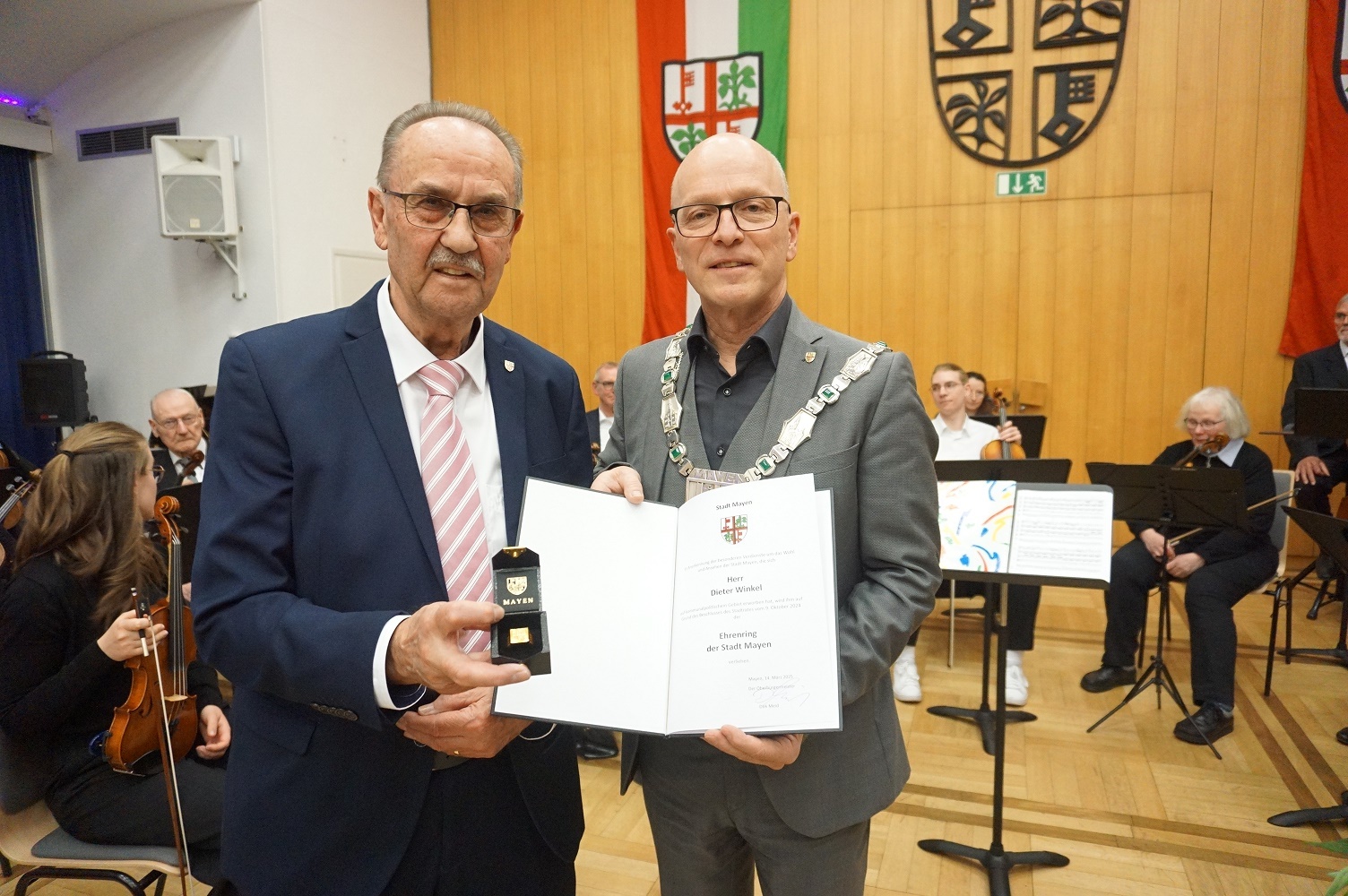 Zwei Männer halten einen Ring und eine Urkunde in den Händen