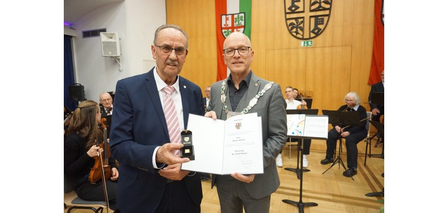 Zwei Männer halten einen Ring und eine Urkunde in den Händen