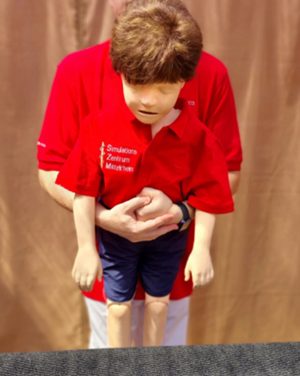 Eine Puppe in einem roten Poloshirt wird von einer Person im Hintergrund gehalten