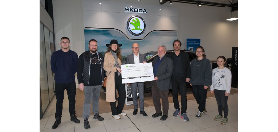 8 Personen stehen für ein Foto zusammen - 3 davon halten einen großen Scheck in der Hand