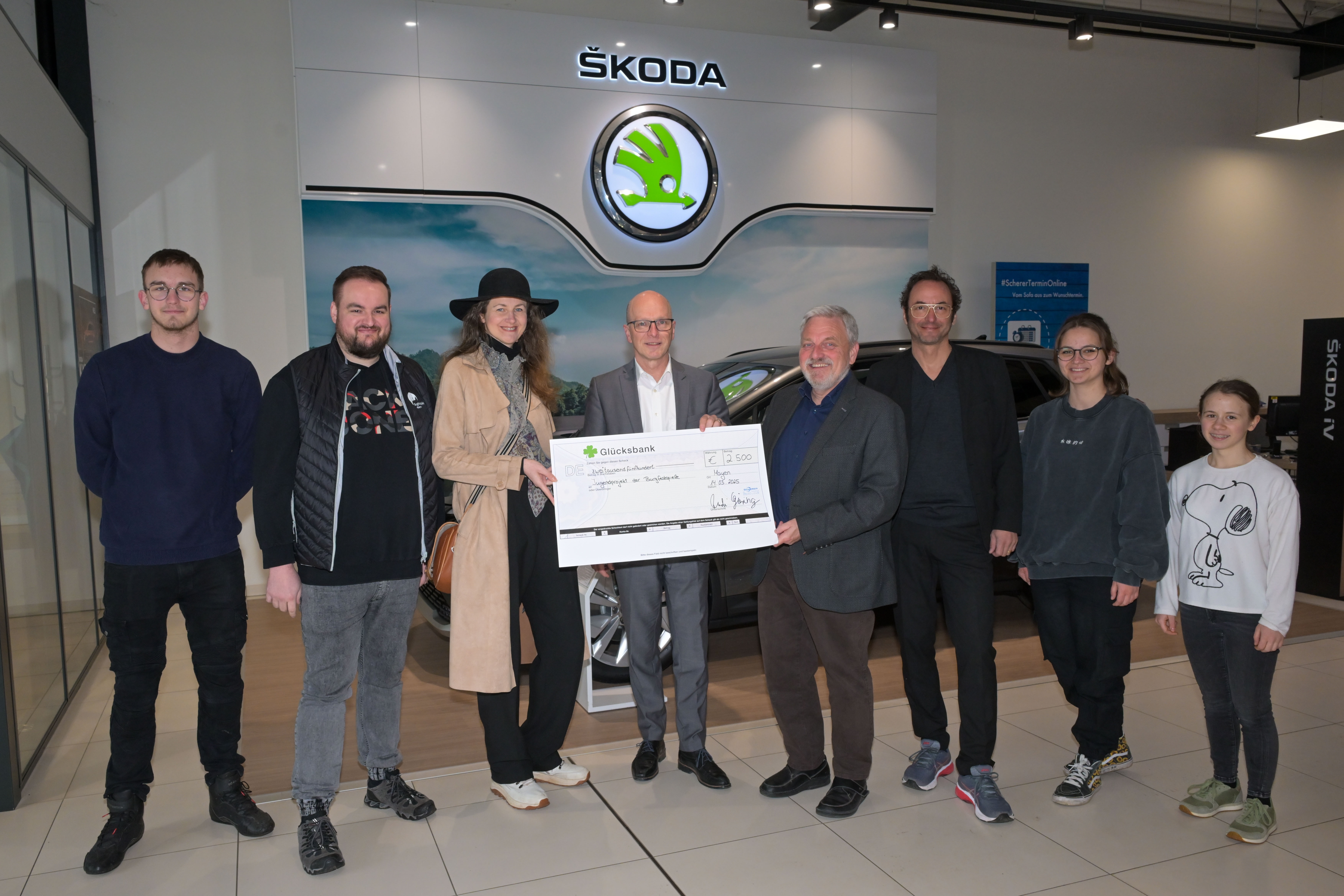 8 Personen stehen für ein Foto zusammen - 3 davon halten einen großen Scheck in der Hand