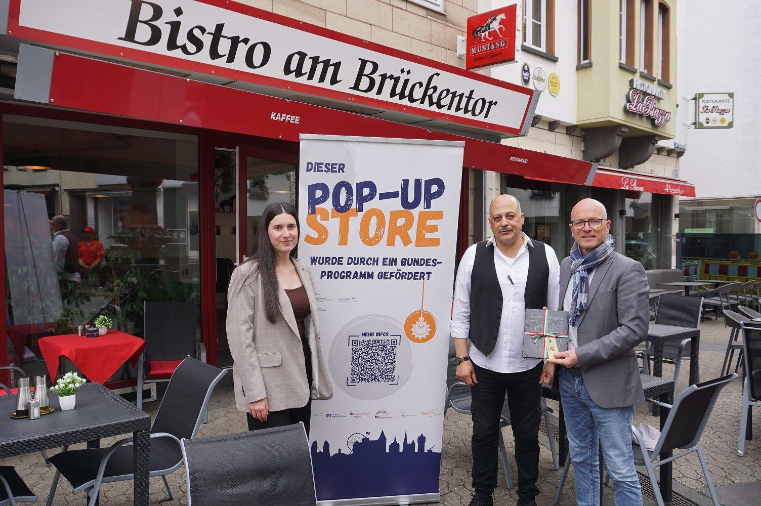 3 Personen und ein Roll-Up stehen vor dem neuen Bistro