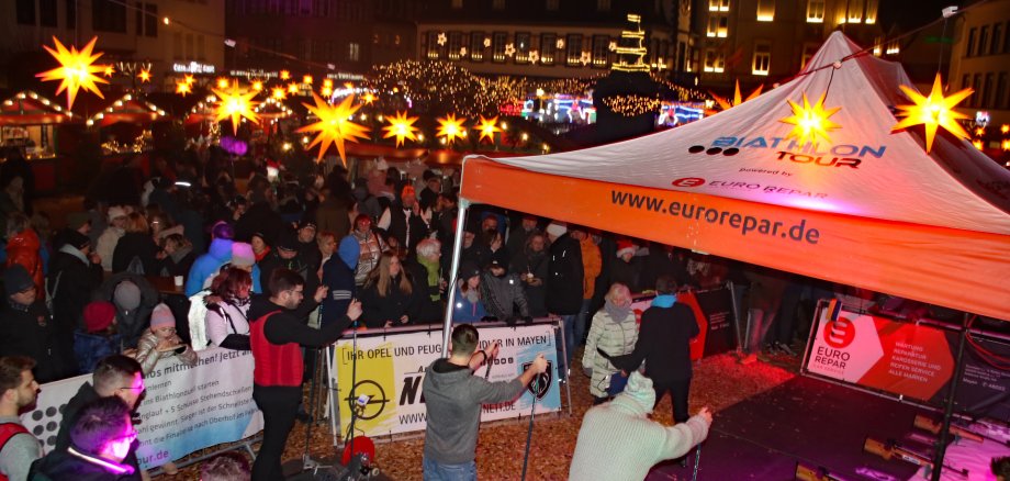 Viele Menschen stehen auf dem weihnachtlich geschmückten Marktplatz und schauen den Sportlern zu.