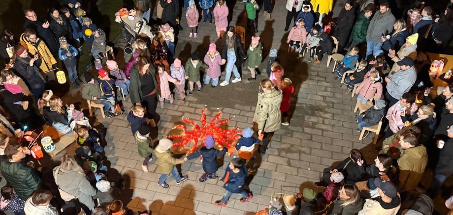 Viele Kinder und Erwachsene stehen zusammen mit ihren bunten Laternen