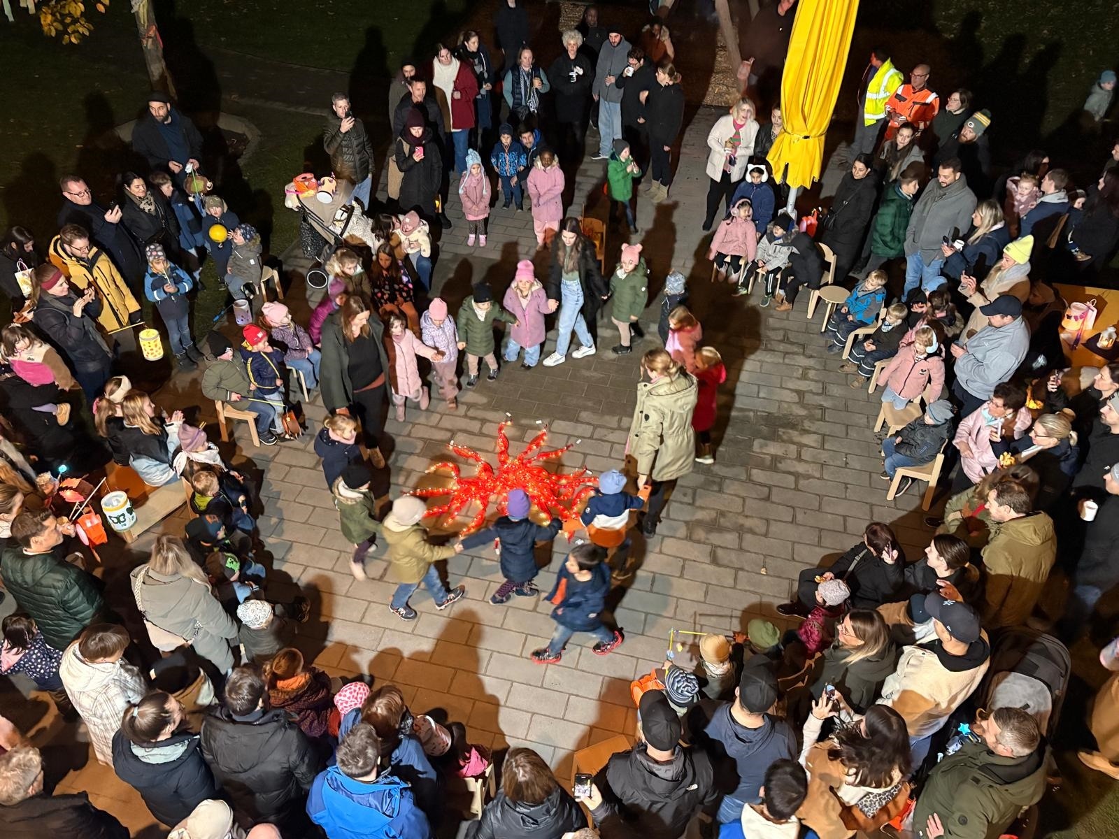 Viele Kinder und Erwachsene stehen zusammen mit ihren bunten Laternen