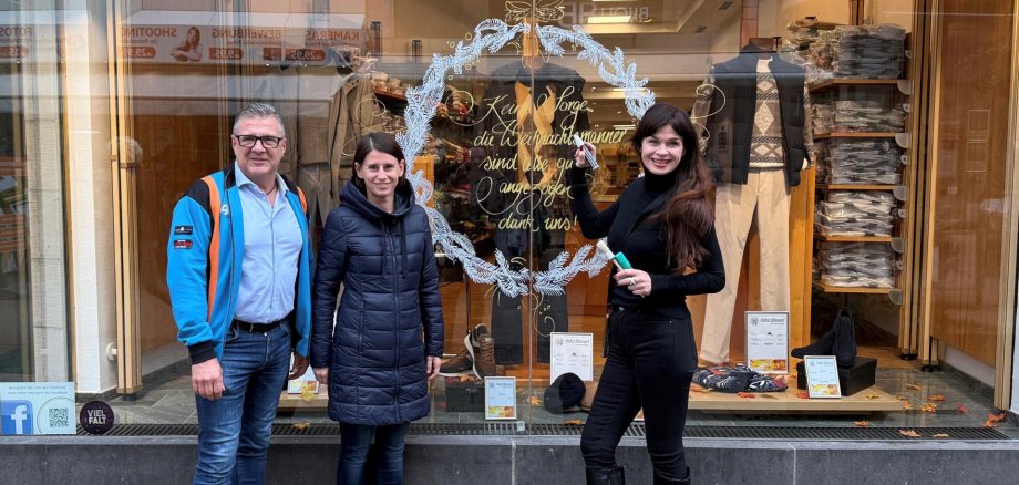 3 Personen stehen in der Innenstadt vor einem bemalen Fenster