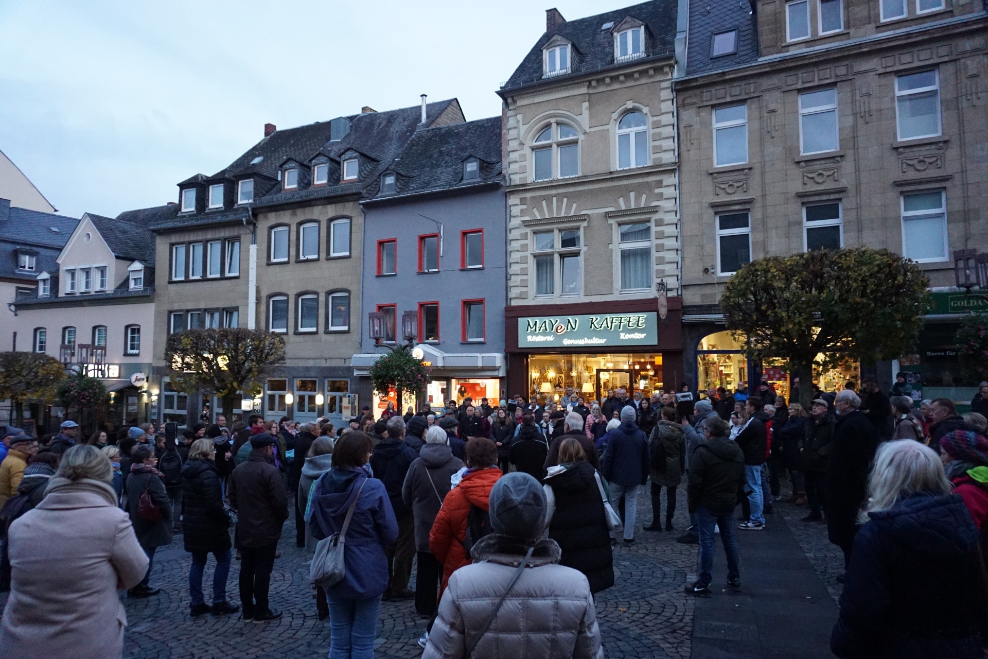 Viele Menschen stehen gemeinsam bei Dämmerung auf dem Marktplatz