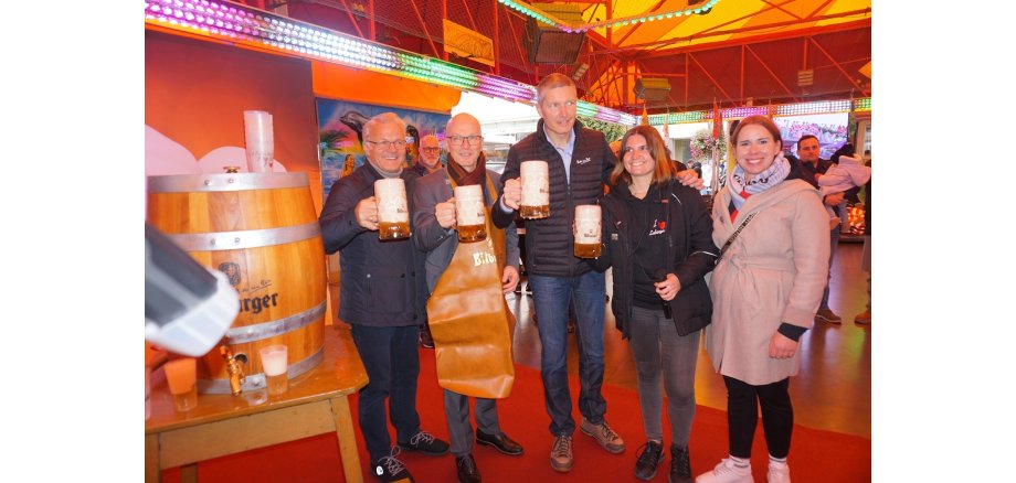 Bereits im letzten Jahr gab es einen Fassanstich am Autoscooter auf dem Marktplatz Fünf Personen stehen auf der Fläche des Autoscooters und haben Bierkrüge in der Hand.