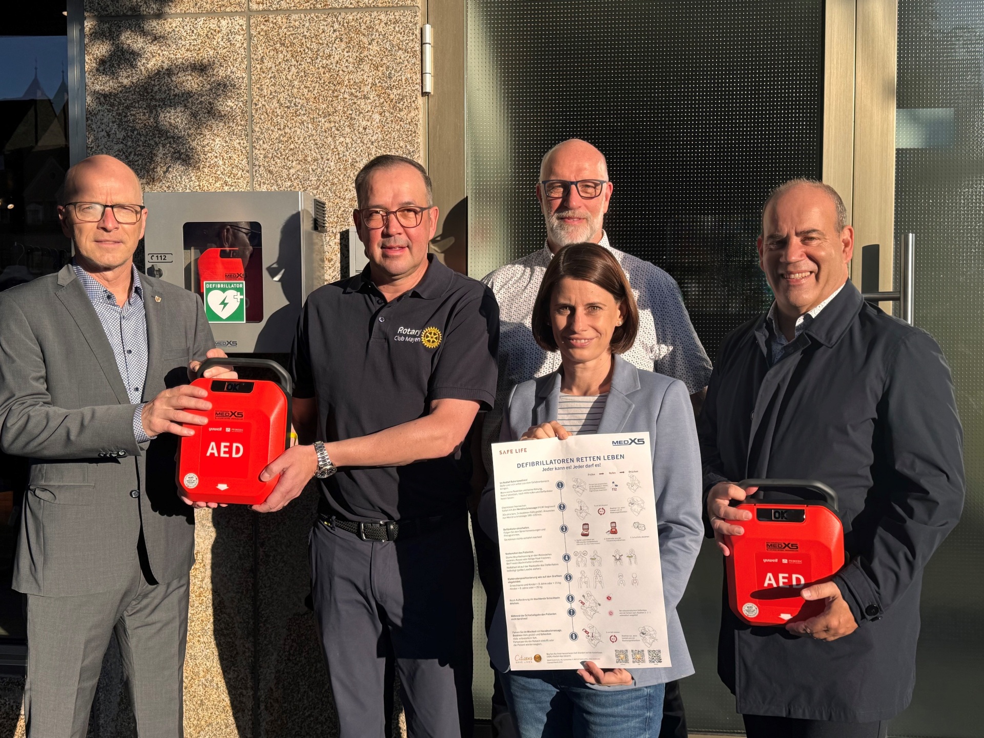 v.l.n.r.: Oberbürgermeister Dirk Meid, Markus Schmitt, Präsident des Rotary Club Mayen 2024/2025, Christina Wolff von der Wirtschaftsförderung, Fachbereichsleiter 1, Uwe Hoffmann und Bernd Faber von Faber Fachgroßhandel (verantwortlich für die Beschaffung der AEDs) bei der Übergabe eines AED vor dem Modehaus Küster