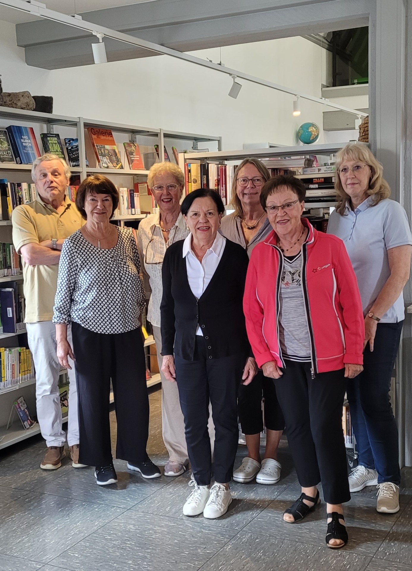 Die ehrenamtlichen Helferinnen und Helfer der Stadtbücherei stehen gemeinsam in der Bücherei vor mit Büchern gefüllten Regalen