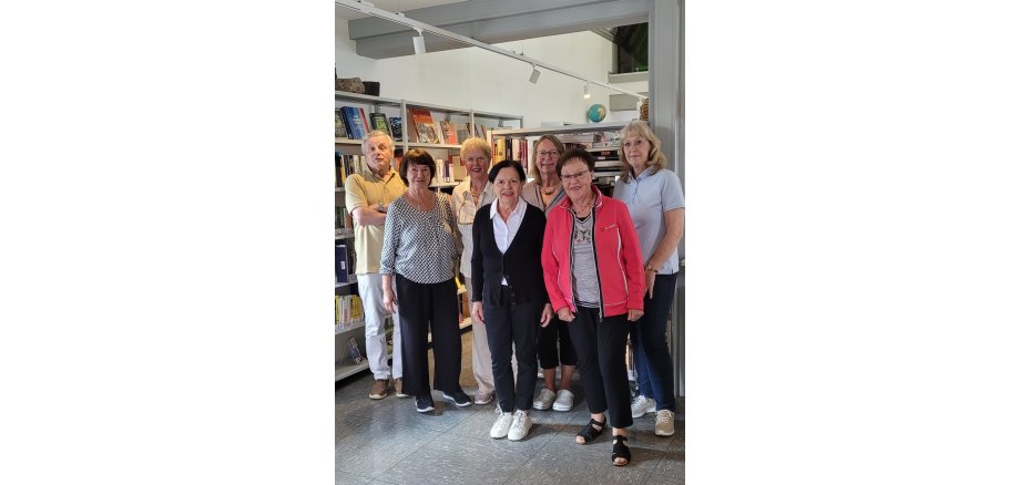 Die ehrenamtlichen Helferinnen und Helfer der Stadtbücherei stehen gemeinsam in der Bücherei vor mit Büchern gefüllten Regalen