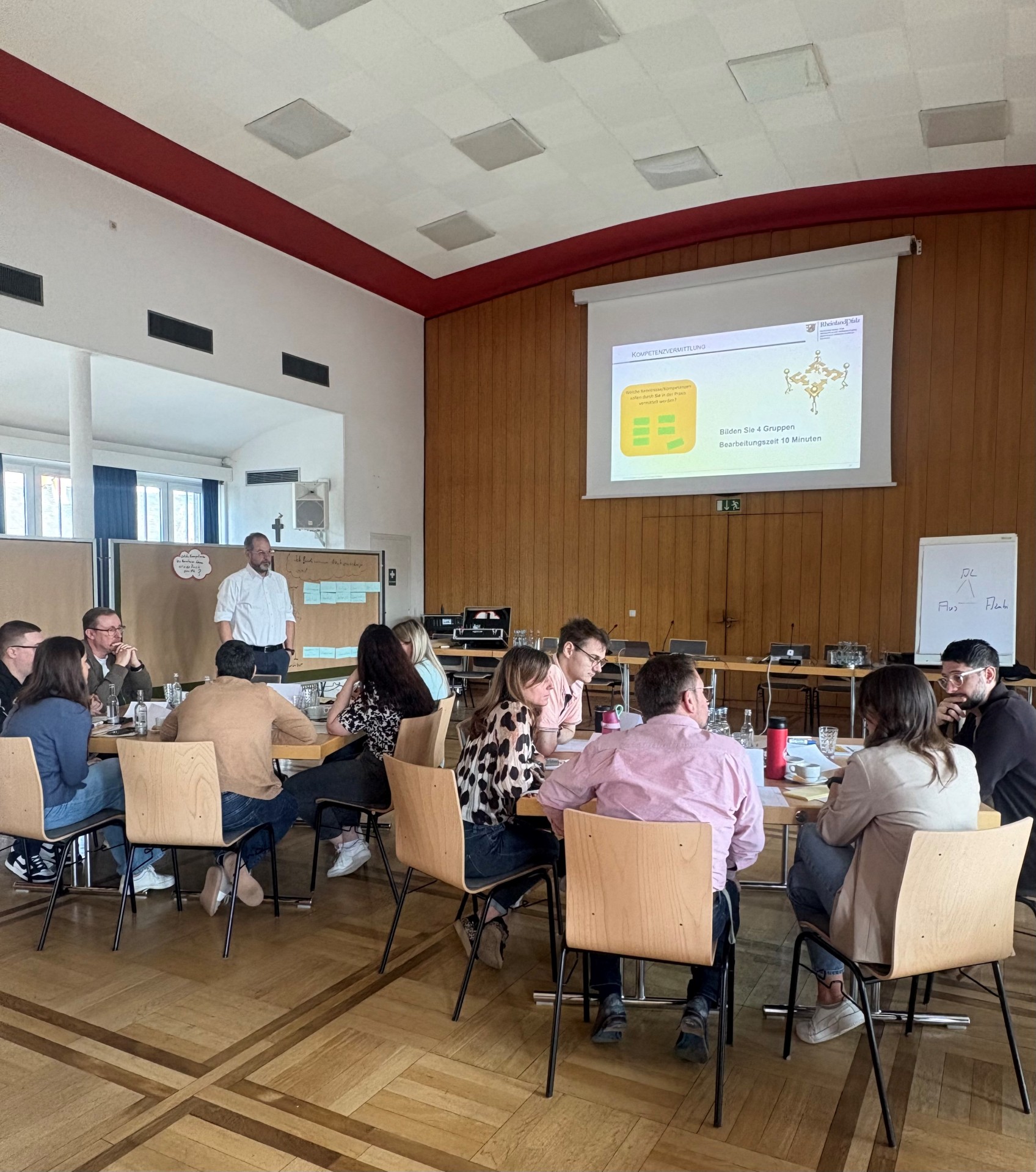 Die Ausbilder sitzen an Gruppentischen und hören den Dozenten zu