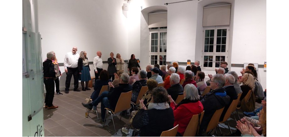 Mehrere Menschen stehen vor einer Gruppe sitzender Menschen und tragen etwas vor