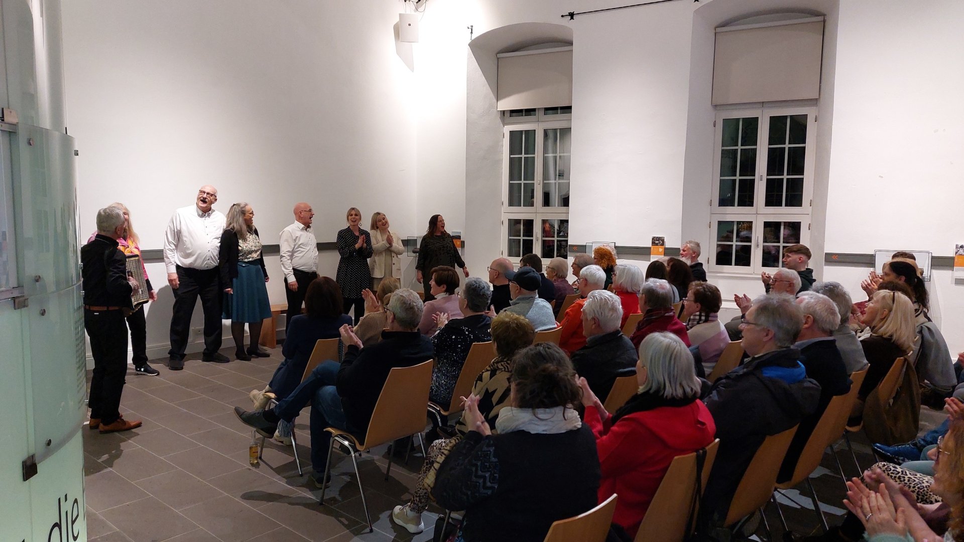 Mehrere Menschen stehen vor einer Gruppe sitzender Menschen und tragen etwas vor