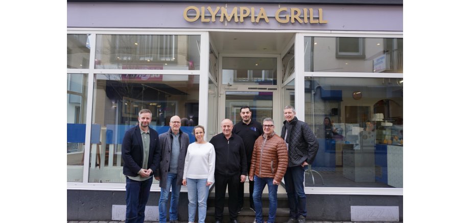 7 Personen stehen vor dem Eingang des Olympia Grills