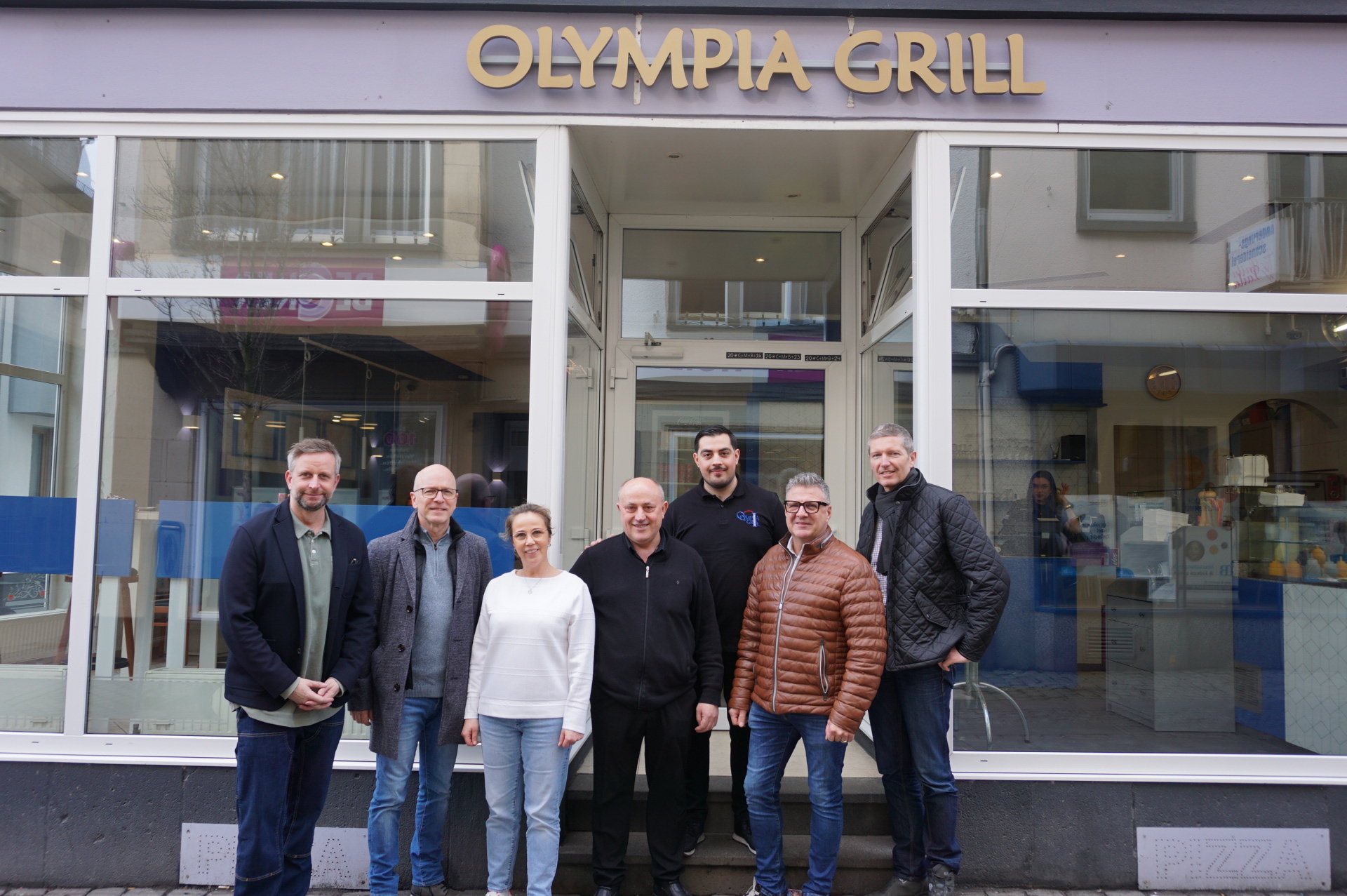 7 Personen stehen vor dem Eingang des Olympia Grills