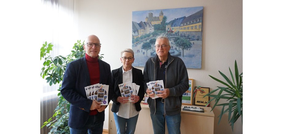 v.l.n.r.: Oberbürgermeister Dirk Meid, Leona Ockenfeld von der Geschäftsstelle VHS und der pädagogische Leiter der VHS Josef Brodam 3 Personen stehen zusammen und halten Hefte in den Händen