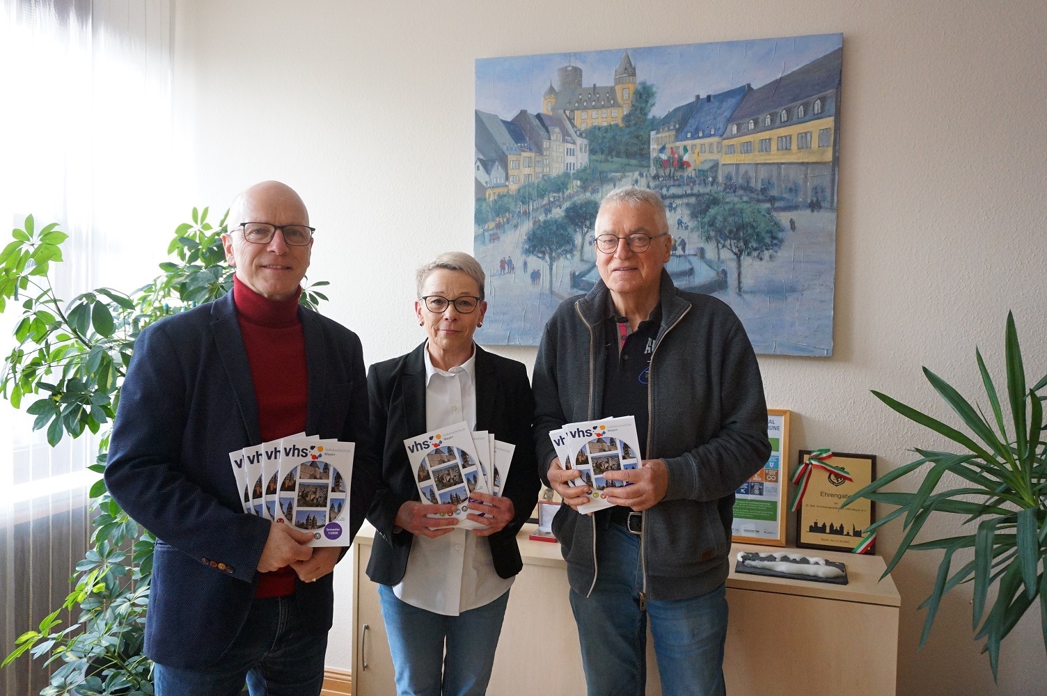 3 Personen stehen zusammen und halten Hefte in den Händen