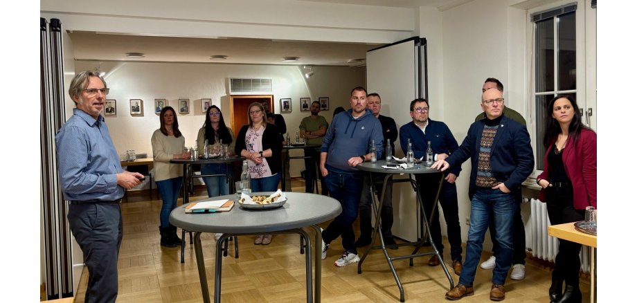 In gemütlicher Atmosphäre erläuterte Dr.-Ing. Dierk Deußen verschiedene Inhalte zum Thema „Moderne Führung“ Die Führungskräfte stehen versammelt in einem Raum und hören aufmerksam zu