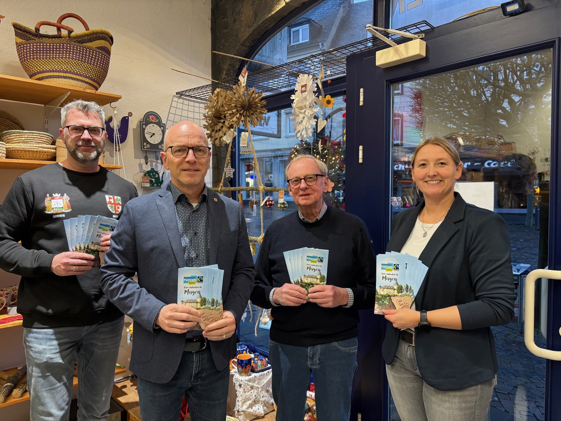 Oliver Schick (Steuerungsgruppe Fairtrade), Oberbürgermeister Dirk Meid, Harald Viehmann (Steuerungsgruppe Fairtrade) und Fairtrade Beauftragte Janine Pitzen stehen nebeneinander im eine Welt Laden und halten gemeinsam jeweils einen Flyer in der Hand
