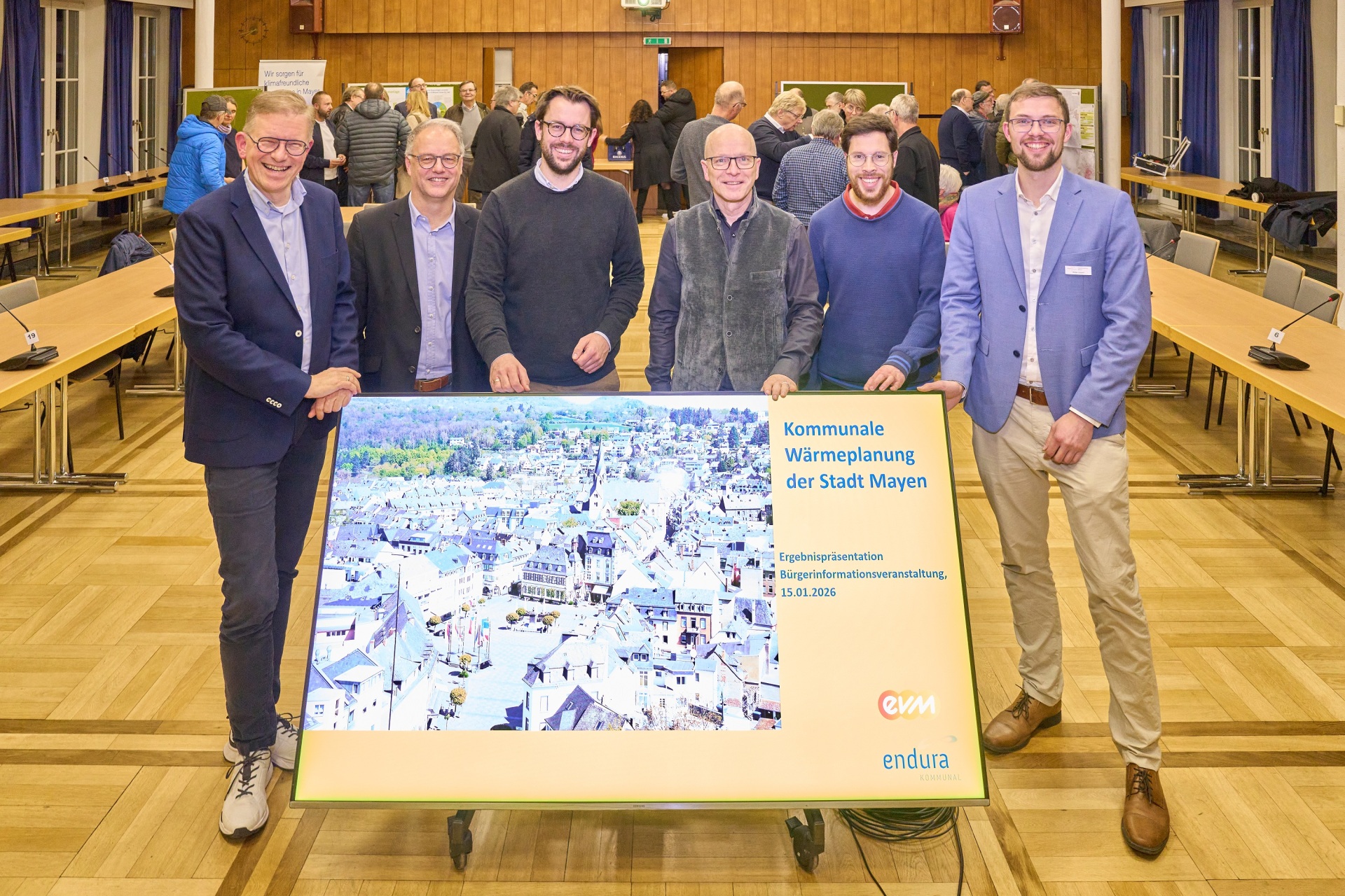 Sechs Männer stehen gemeinsam im Sitzungssaal der Stadtverwaltung hinter einem Schild mit dem Wärmeplan