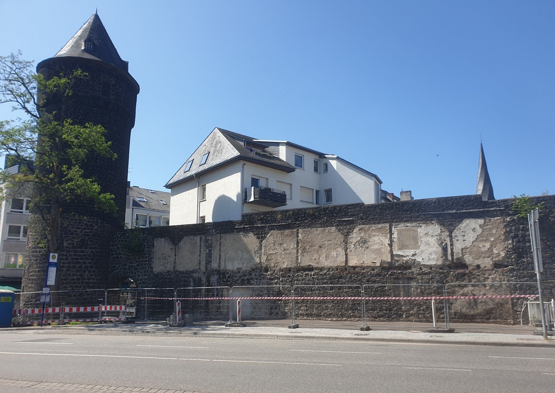 Mühlenturm mit Stadtmauer vor der ein Bauzaun steht.