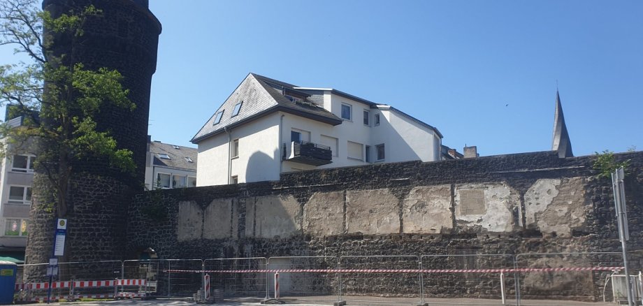 Mühlenturm mit Stadtmauer vor der ein Bauzaun steht.