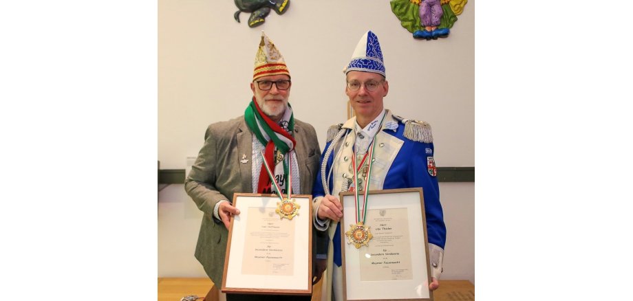 Die Ordensträger Uwe Hoffmann und Udo Thielen stehen nebeneinander im Museum und halten Stolz ihre Urkunden und Orden in der Hand