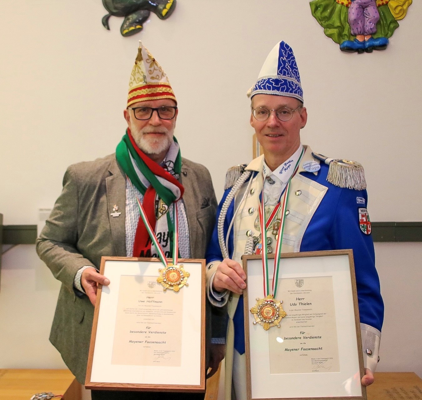 Die Ordensträger Uwe Hoffmann und Udo Thielen stehen nebeneinander im Museum und halten Stolz ihre Urkunden und Orden in der Hand