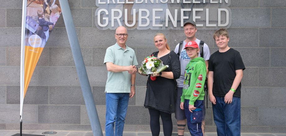 600.000 Besucher: Oberbürgermeister Meid ehrt stellvertretend einen Gast auf dem diesjährigen Römerfest Drei Erwachsene und zwei Kinder stehen vor den Erlebniswelten Grubenfeld