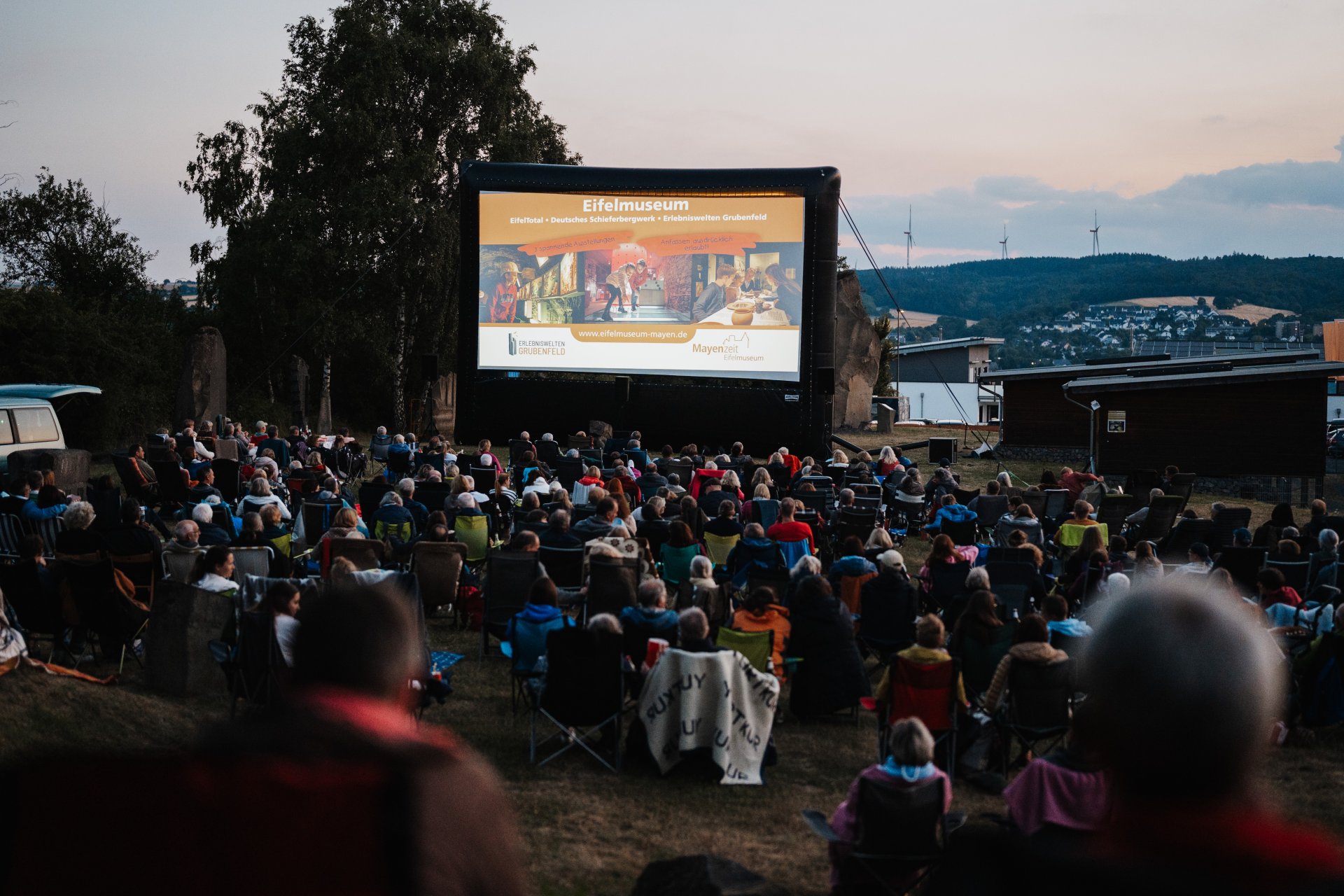 Große Leinwand draußen vor der viele Besucher sitzen