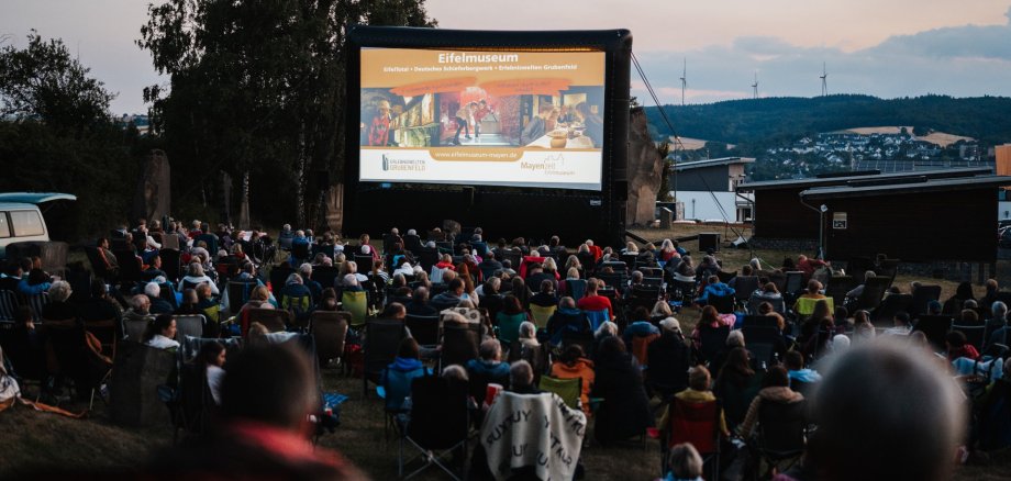 Vorpremiere von „Chéri, ich komme! – Die Erfindung der Lust“ beim Open-Air-Kino auf dem Grubenfeld Große Leinwand draußen vor der viele Besucher sitzen