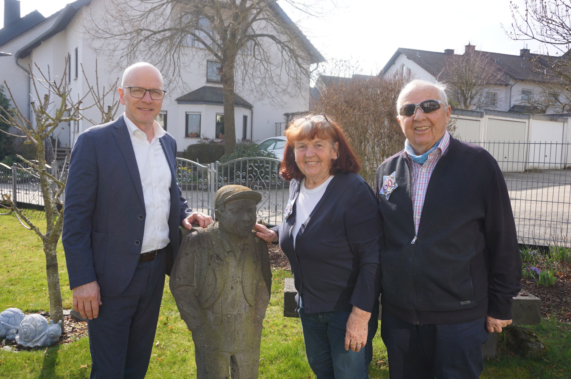 Oberbürgermeister Dirk Meid  steht draußen mit Margarete und Bernd Rothbrust. Neben ihnen steht eine Figur vom Mayener Jung.