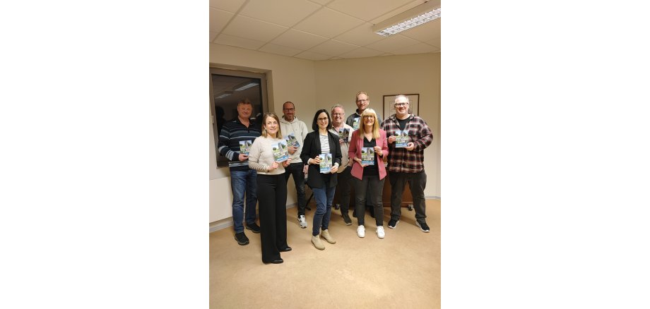 Acht Menschen stehen zusammen und halten jeweils eine Informationsbroschüre in den Händen