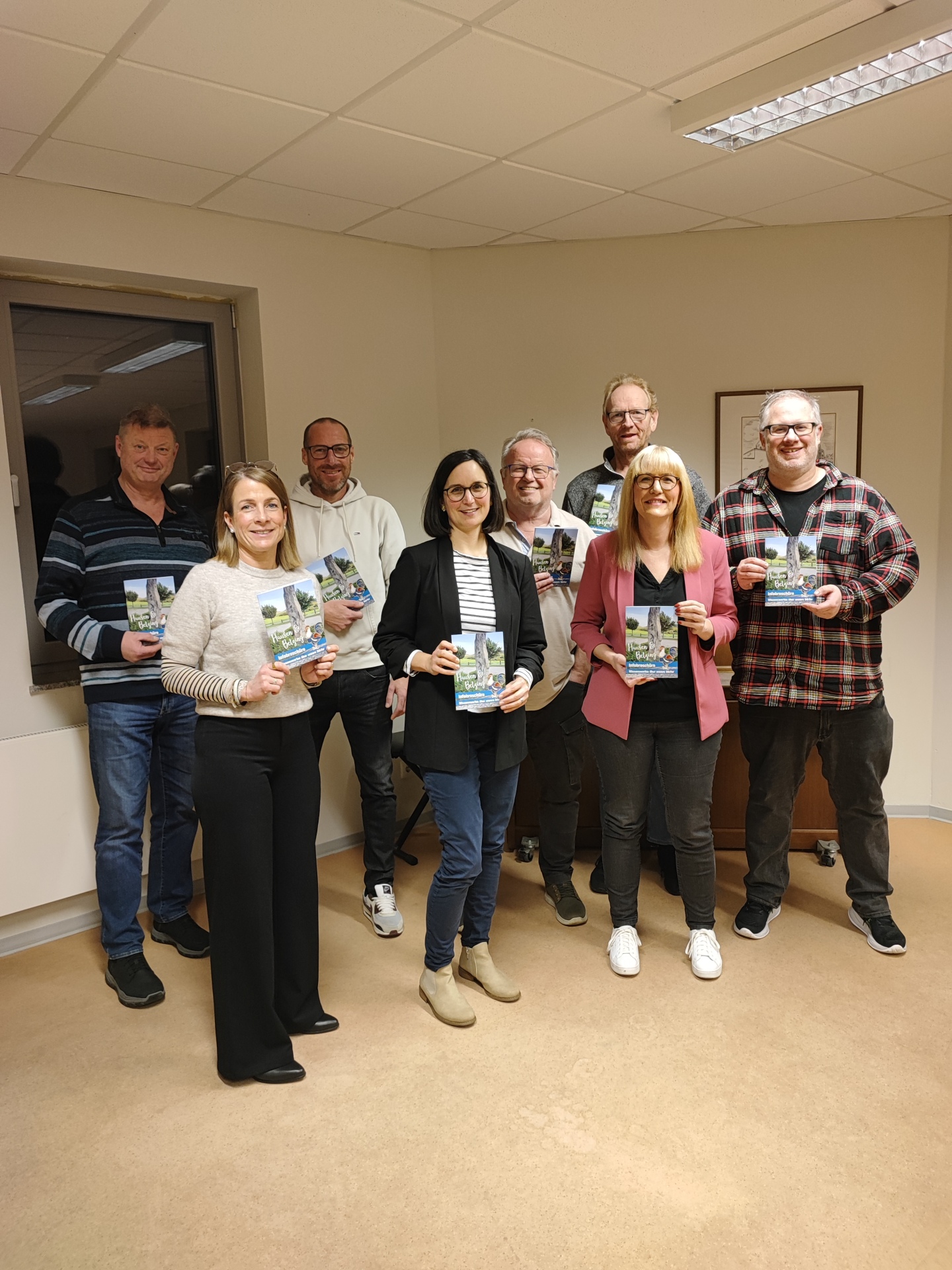 Acht Menschen stehen zusammen und halten jeweils eine Informationsbroschüre in den Händen
