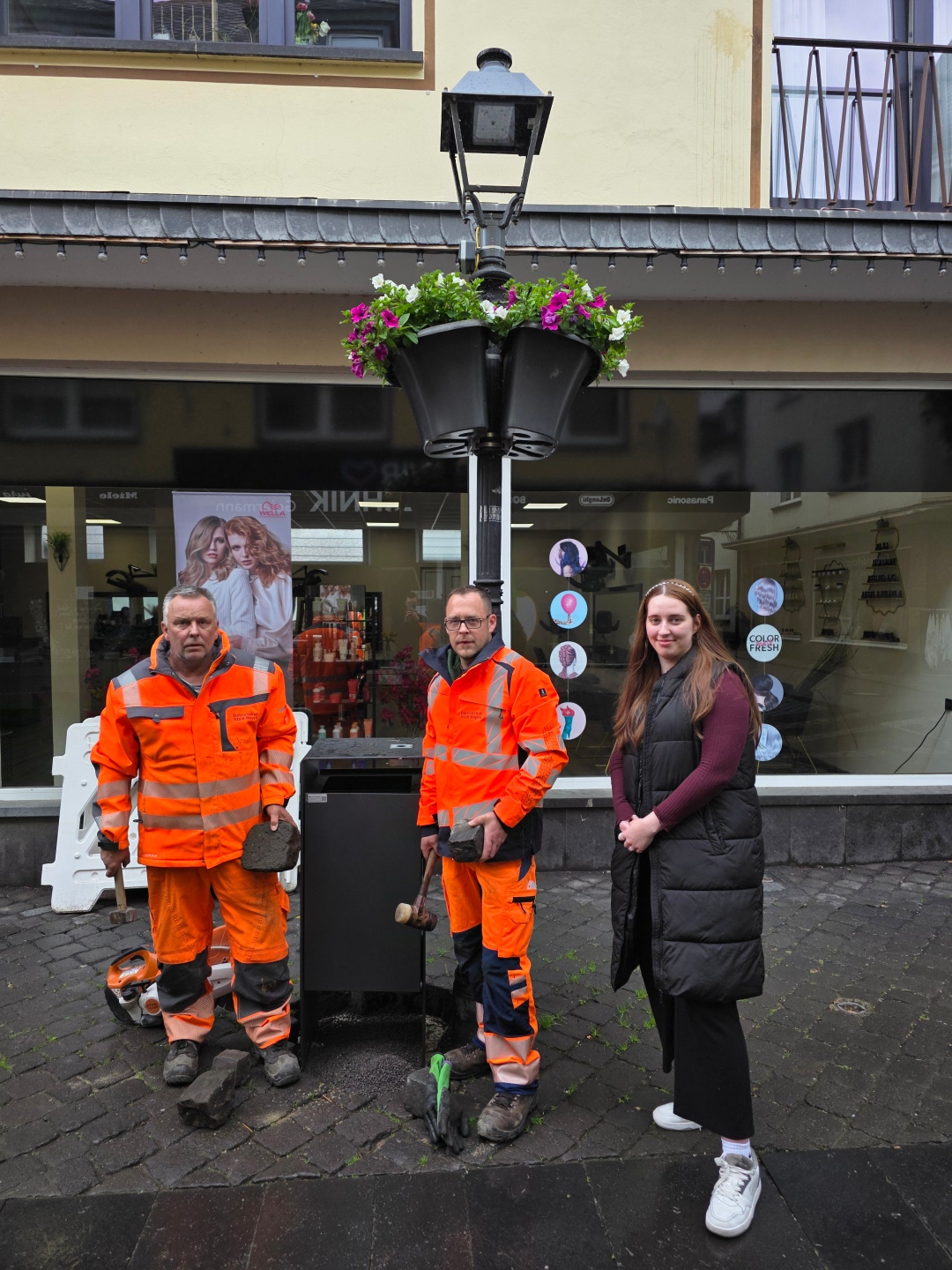 Zwei Mitarbeiter des städtischen Betriebshof und eine Mitarbeiterin der Stadtverwaltung stehen neben einem der neuen Mülleimer