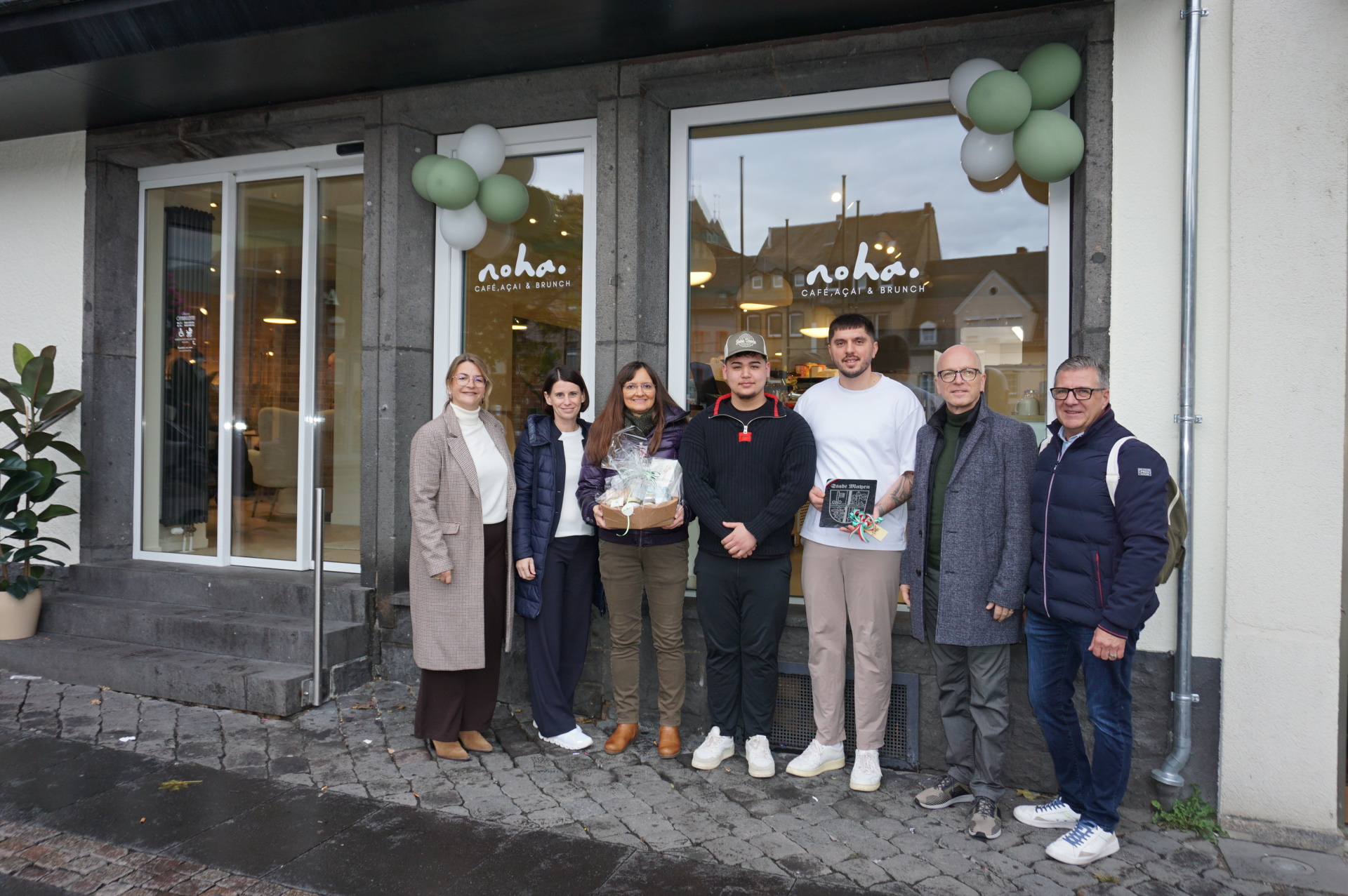 Vertreterinnen und Vertreter der Stadt sowie Eigentümer stehen vor dem Schaufenster vor dem Cafe