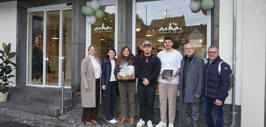 Vertreterinnen und Vertreter der Stadt sowie Eigentümer stehen vor dem Schaufenster vor dem Cafe