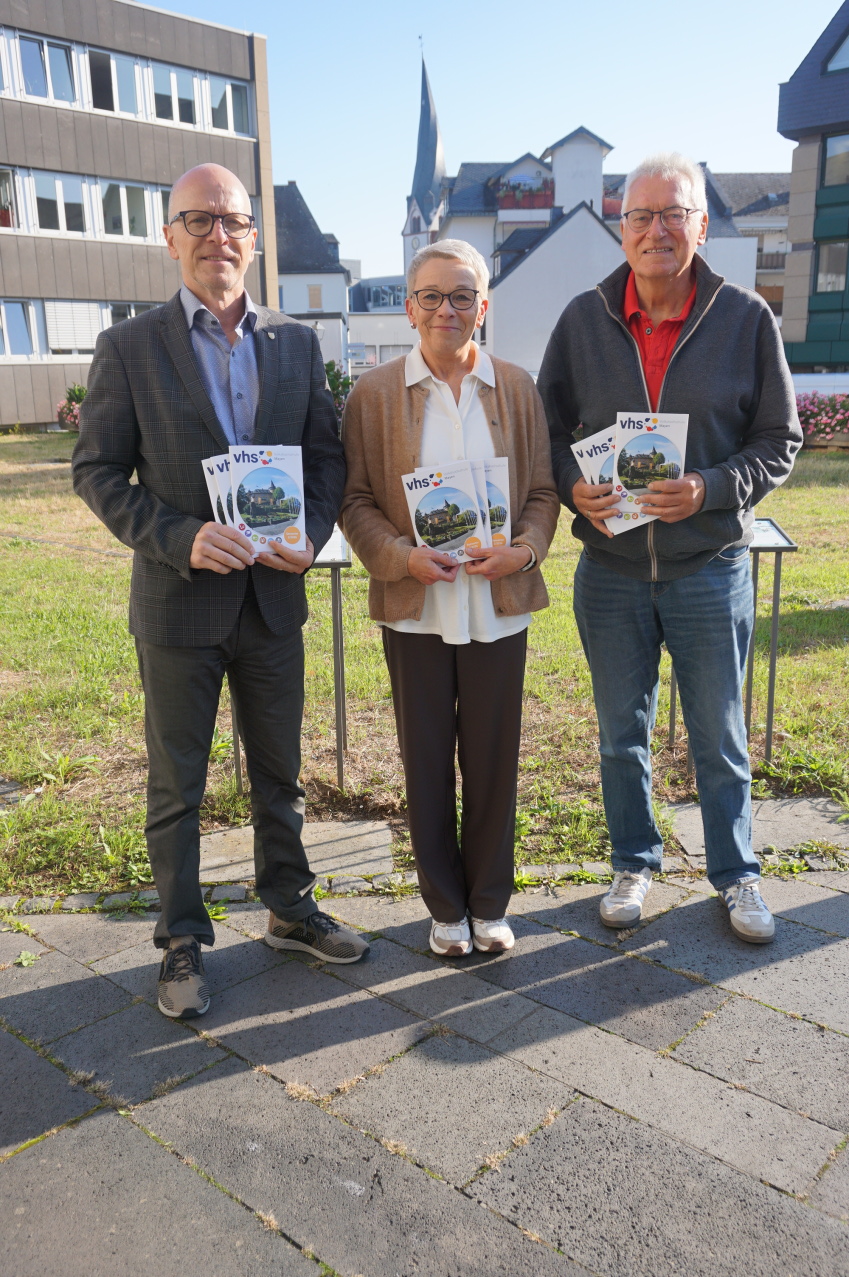 Zwei Männer und eine Frau stehen vor einer Wiese und halten das neue Heft in den Händen