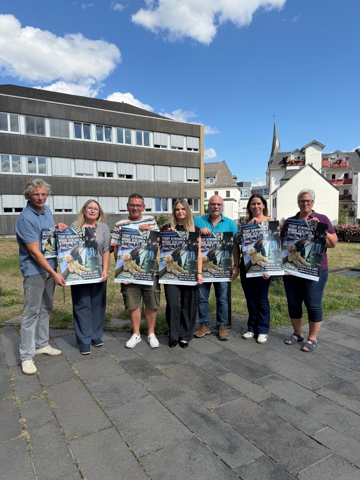 Bernhard Gödert von der Caritas Mayen, Jutta Kruft vom Wochenspiegel, Dirk Schmitz von der Lebenshilfe Mayen, Hanna Mallmann vom Ordnungsamt, Thomas Mintenig vom Jugendamt, Marktmeisterin Yvonne Ditzler und Alexandra Bauer Didaktische Koordinatorin der Realschule Plus in Mayen stehen draußen vor der Verwaltung und halten das neue Plakat in den Händen