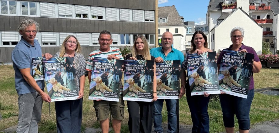 v.l.n.r.: Bernhard Gödert von der Caritas Mayen, Jutta Kruft vom Wochenspiegel, Dirk Schmitz von der Lebenshilfe Mayen, Hanna Mallmann vom Ordnungsamt, Thomas Mintenig vom Jugendamt, Marktmeisterin Yvonne Ditzler und Alexandra Bauer Didaktische Koordinatorin der Realschule Plus in Mayen Bernhard Gödert von der Caritas Mayen, Jutta Kruft vom Wochenspiegel, Dirk Schmitz von der Lebenshilfe Mayen, Hanna Mallmann vom Ordnungsamt, Thomas Mintenig vom Jugendamt, Marktmeisterin Yvonne Ditzler und Alexandra Bauer Didaktische Koordinatorin der Realschule Plus in Mayen stehen draußen vor der Verwaltung und halten das neue Plakat in den Händen