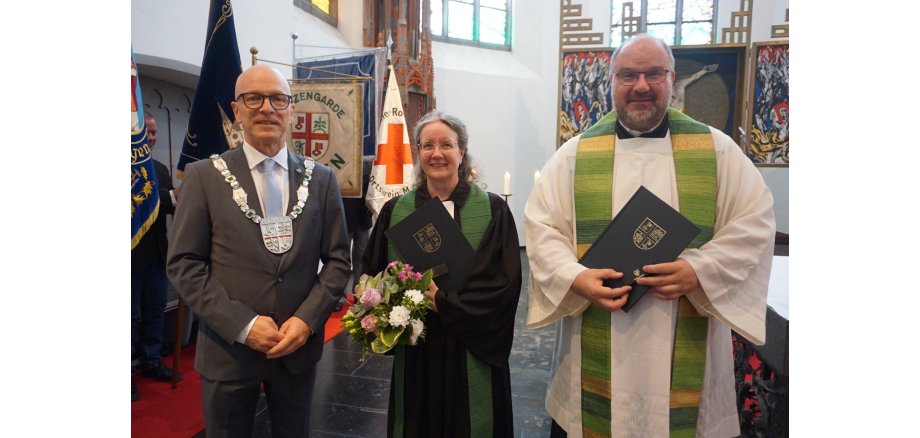 Oberbürgermeister Dirk Meid (links) durfte gleich zwei goldene Ehrennadeln der Stadt Mayen verleihen Oberbürgermeister Dirk Meid steht links neben Pfarrerin Metje Steinau und Dekan Jörg Schuh in einer Kirche