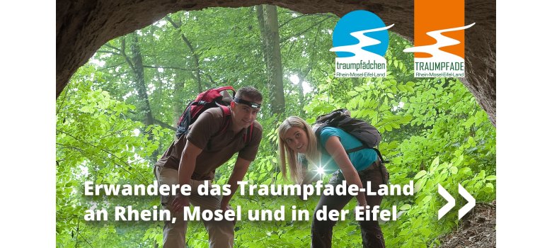 Viele Traumpfade und Traumpfädchen laden in atemberaubende Regionen ein 2 Personen stehen in Wanderausrüstung im Wald vor einer Höhle