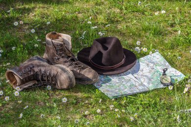 Wanderschuhe, Karte und Hut liegen auf einer Wiese