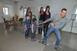 Eine Familie testet ein Ausstellungsstück im Eifelmuseum, bei dem man an einem Zug ziehen kann und die entsprechende Kraft in PS angegeben bekommt. 