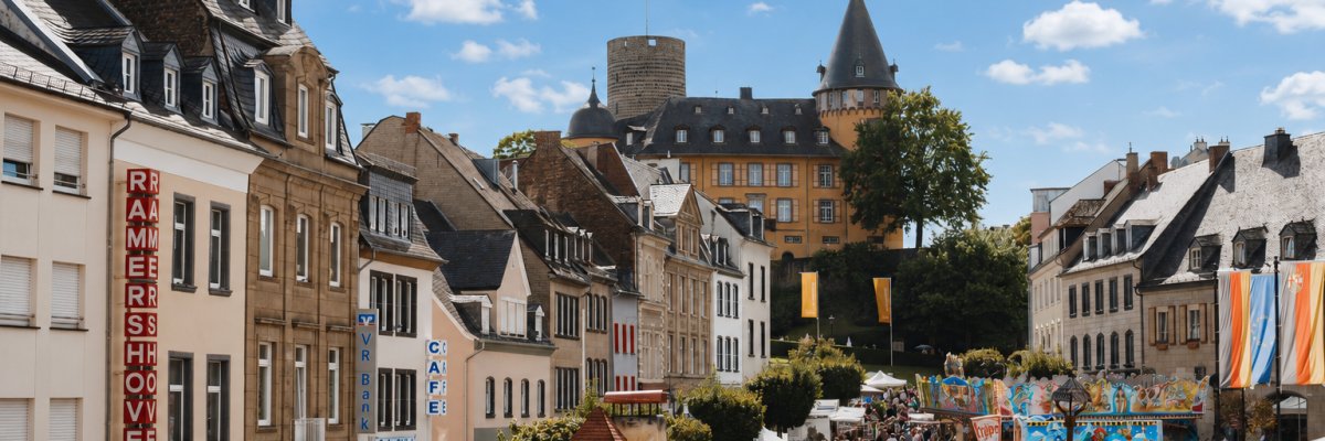 Belebter Marktplatz mit Ständen und Festzelt, im Hintergrund die Genovevaburg